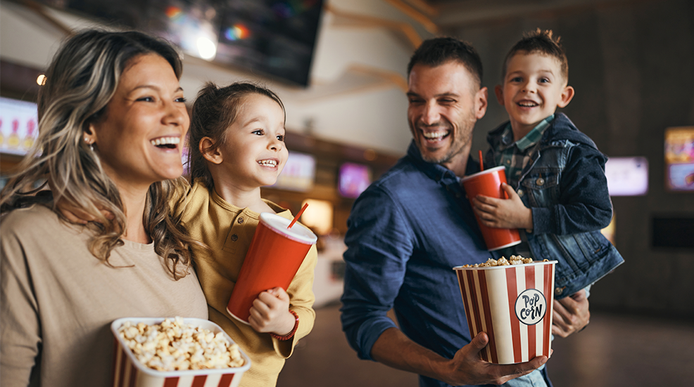 Young happy family with popcorn and drinks in movie theatre